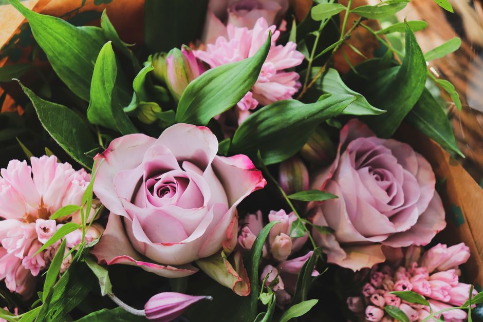 A close-up floral arrangement featuring light pink roses with tightly curled petals displaying a subtle gradient from soft pink to darker pink edges, complemented by clusters of pink hyacinths with sm
