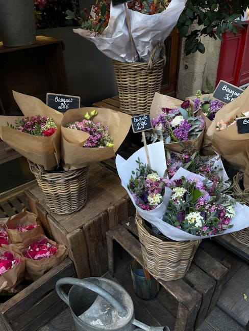 A display of fresh flower bouquets arranged in woven wicker baskets at an outdoor floral shop, featuring an assortment of pastel and vibrant-colored flowers such as pink, purple, white, and green. The